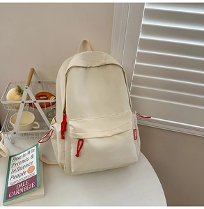 Detail view of a beige minimalist nylon backpack with a red knot zipper and side pocket