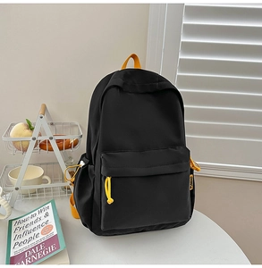 Detail of minimalist black backpack featuring vibrant yellow zipper pull and side drawstring
