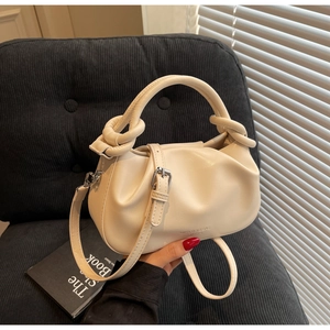 Close-up of cream pleated cloud bag with elegant knot handle and silver brand logo
