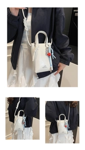 White mini tote bag featuring knotted rope straps and heart charm detail on a leather surface