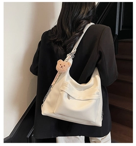 Detail of a large cream hobo tote bag with a plush bear charm on a female model