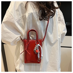 Detail view of a red patent leather mini crossbody bag with embossed logo and metal charms