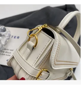 Detailed macro view of white leather handbag featuring gold embroidery and polished metal hardware