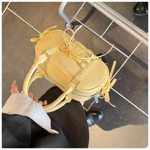 Detail view of yellow patent leather Boston bag with decorative ribbons and metal zipper