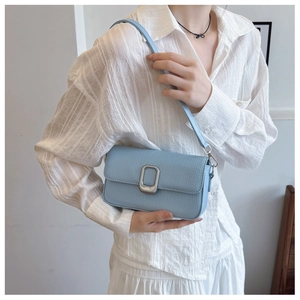 Detail of light blue crossbody bag with silver buckle worn over a white striped shirt