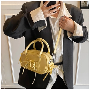 Detail of a bright yellow Boston bag featuring bow tie accents and silver hardware