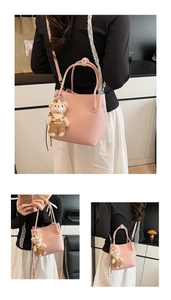 Detail of pink lychee grain leather bucket bag featuring a cute bear bag charm