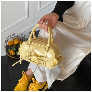 Detailed macro view of vibrant yellow patent leather boston bag with ribbon bow and silver buckle