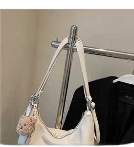 Close-up of white soft leather tote bag with a brown teddy bear charm on metal stand