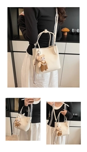 Close-up of cream textured leather bucket bag with a cute bear pendant and top handle