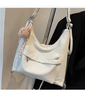 Close-up of white lychee-grain hobo bag featuring a plush bear and decorative scarf