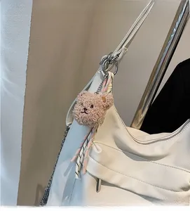 Detail of white lychee leather tote bag with brown plush bear charm and metal chain