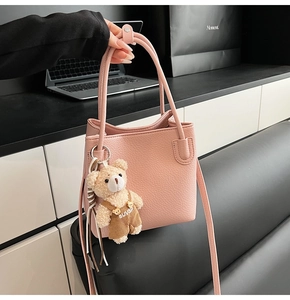 Detail of pink lychee leather bucket bag featuring a cute brown plush bear charm and straps