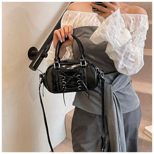 Detail of black patent leather Boston bag with corset lace-up design and silver eyelets