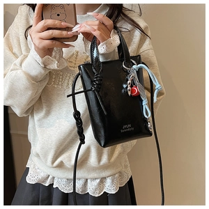 Close-up of black patent leather crossbody bag with decorative charms and knotted strap