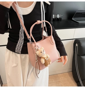 Pink bucket bag with lychee texture featuring a cute teddy bear charm worn as crossbody