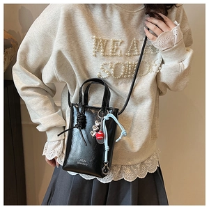 Detail view of black glossy leather crossbody bag with charms and JYUN logo on grey sweater