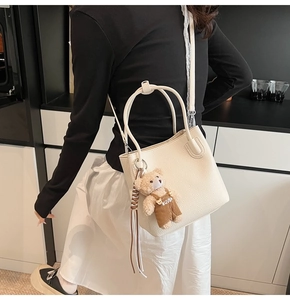Detail of cream white lychee leather bucket bag with a cute plush bear charm accessory
