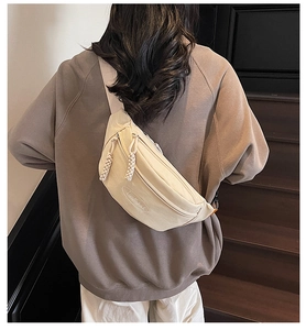 Detail of beige canvas crossbody bag with woven rope zipper on a grey sweatshirt