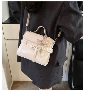 Detail view of beige crossbody bag with ribbon bow and pearl heart charm on grey blazer