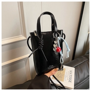 Detail of black glossy leather mini tote bag with white lettering and decorative charms