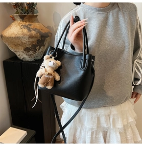 Detail of black pebbled leather bucket bag with cute teddy bear charm and shoulder strap