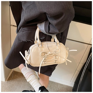 Detail of a creamy white Boston bag featuring cross-laced bow design and glossy finish