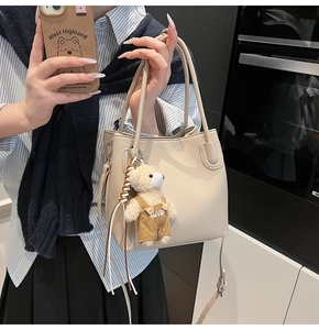 Detail view of a beige lychee texture bucket bag featuring a cute bear plush pendant