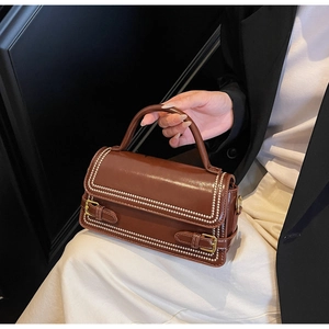 Detailed view of brown leather square handbag with white pearl trim and gold buckle accents