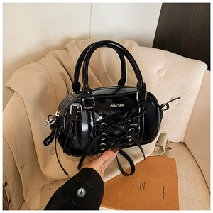 Detail of black patent leather Boston bag with ribbon lace-up design and silver eyelets