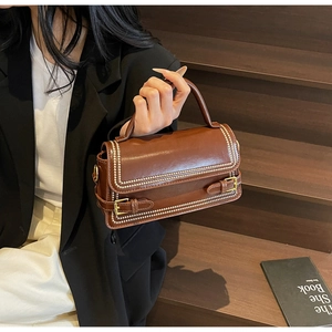 Detailed macro view of the brown leather handbag showing golden rivet accents and buckle