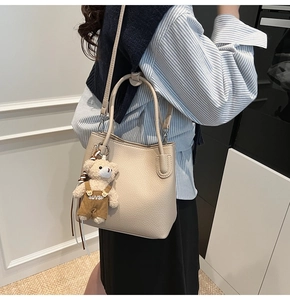 Detail of cream white lychee leather bucket bag with a cute bear charm and shoulder strap