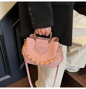 Pink lychee grain leather bucket bag featuring a U-shaped gold metal handle and chain strap