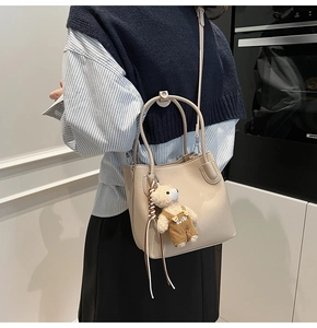 Detail of cream pebbled leather bucket bag featuring a cute plush bear charm with adjustable strap