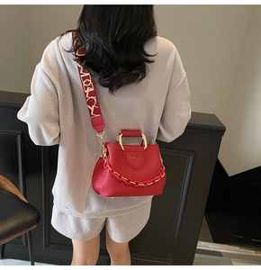 Detail of red lychee leather handbag featuring decorative gold chain and woven jacquard strap