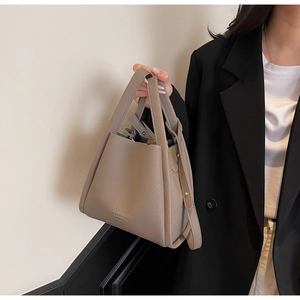 Detail of taupe lychee texture leather bucket bag with embossed logo on model