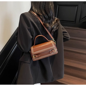 Detail of vintage dark brown faux leather crossbody bag with white stitching and buckles