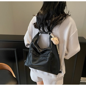 Detail view of black textured leather tote with plush bear charm and striped ribbon accent