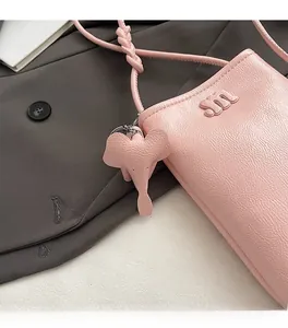 Detail of pink lychee leather crossbody phone bag with m logo and elephant charm