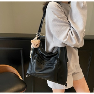 Detail of black pebbled leather hobo bag with front pocket and plush bear charm
