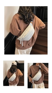 Detail of light grey nylon crescent bag with orange buckle and white woven zipper pull