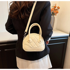 Detail of quilted creamy white shell handbag with round top handles and metal crossbody strap