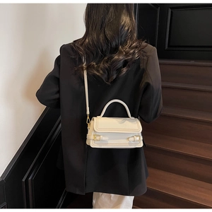 Detail of cream leather crossbody bag with metal buckle straps on dark wood stairs