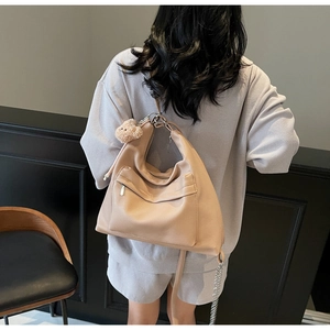 Close-up of beige lychee grain leather tote bag with cute bear charm and chain strap