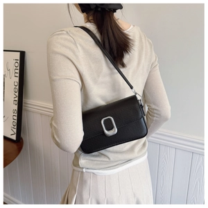 Detail of minimalist black pebbled leather handbag featuring oval silver metallic clasp
