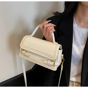 Detail of cream leather square bag featuring golden braided stitching and metal buckles