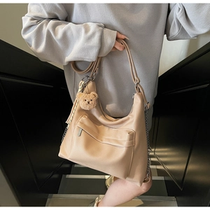 Detail of beige faux leather tote with plush bear charm and metallic chain accent