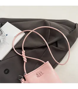 Close-up of pink pebbled leather crossbody bag with 3D letter M logo on grey suit fabric