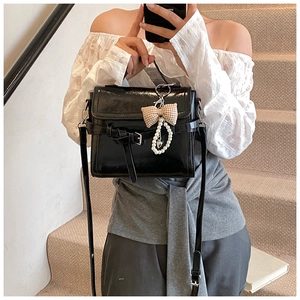 Detail of black faux leather handbag with belt buckle, plaid bow, and pearl chain