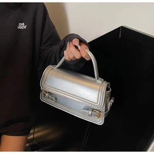 Detail of silver handbag with metallic finish, contrast stitching, and metal buckle straps